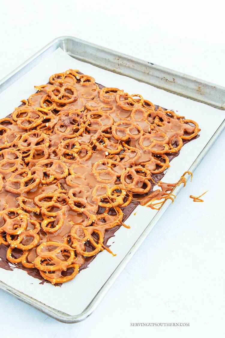 Chocolate, pretzels, and caramel layered on a parchment paper-lined cookie sheet.