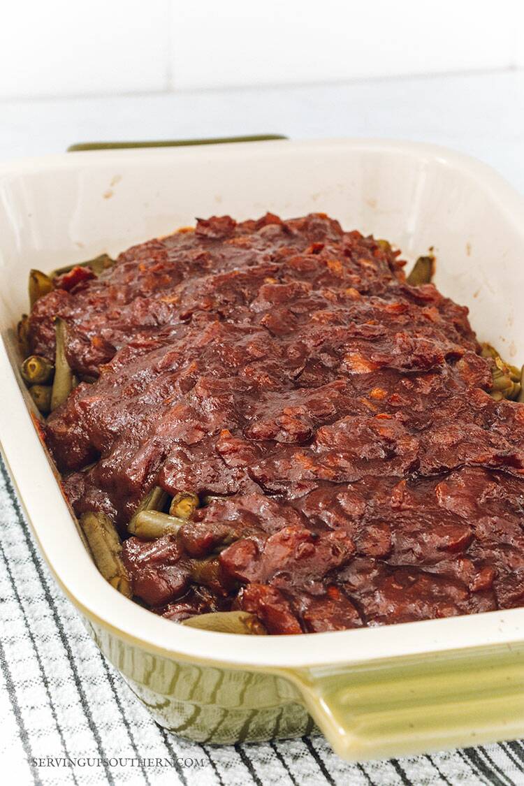 Baking dish filled with barbecued green beans sitting on a tea towel.