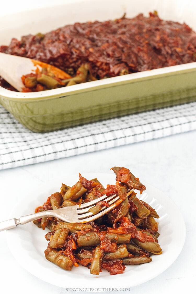 A plate of barbecued green beans sitting on a white surface with serving dish in the background.