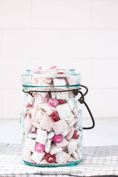 A blue ball jar filled with strawberries and cream puppy chow snack sitting on a marble surface.