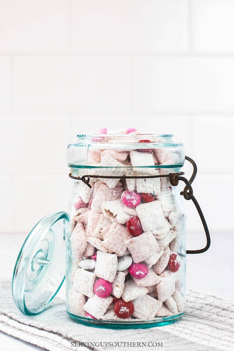 A blue ball jar filled with strawberries and cream puppy chow snack sitting on a marble surface.