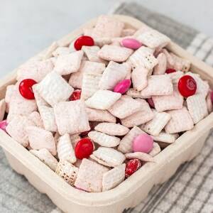 A berry basket filled with strawberries and cream puppy chow snack setting on a marble surface.