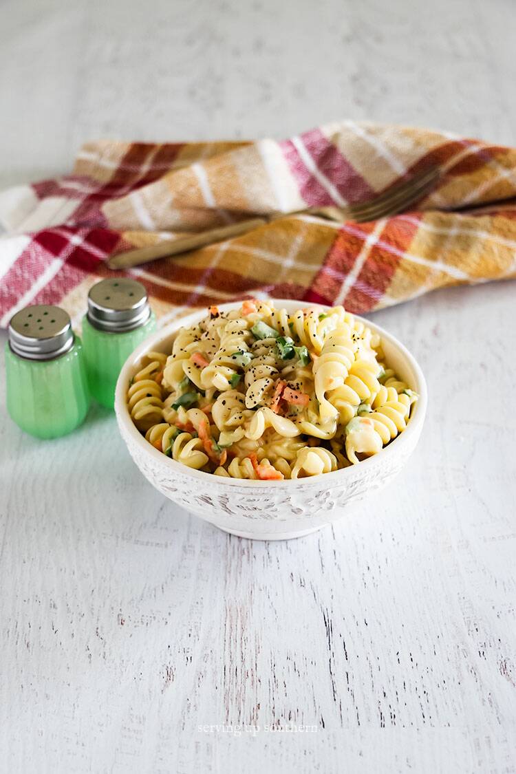 Amish macaroni salad with twisted noodles in a white bowl on a rustic chippy wood board.
