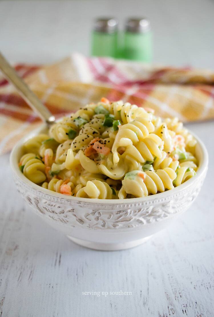 Amish - Macaroni Salad in a white bowl on a white rustic wooden board.