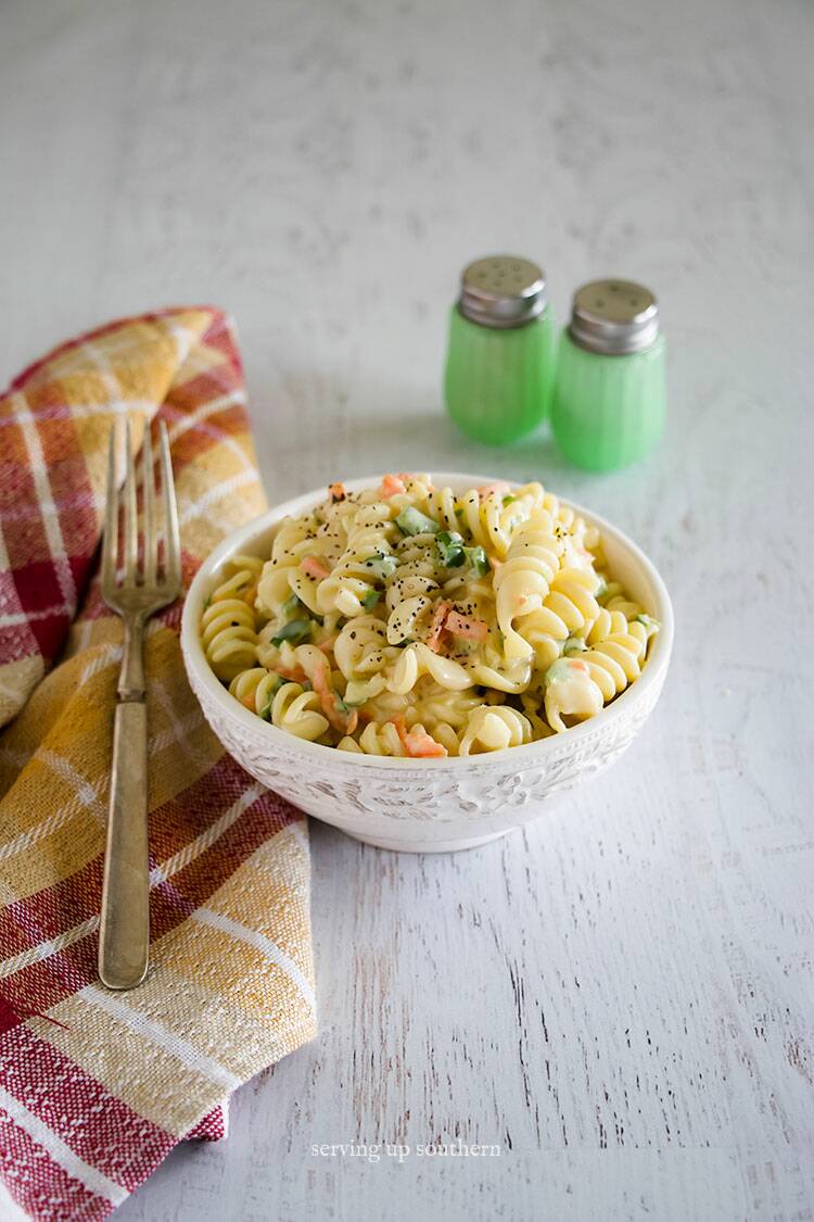 Amish Macaroni Salad in a white bowl on white rustic wooden board with a fork and napkin.