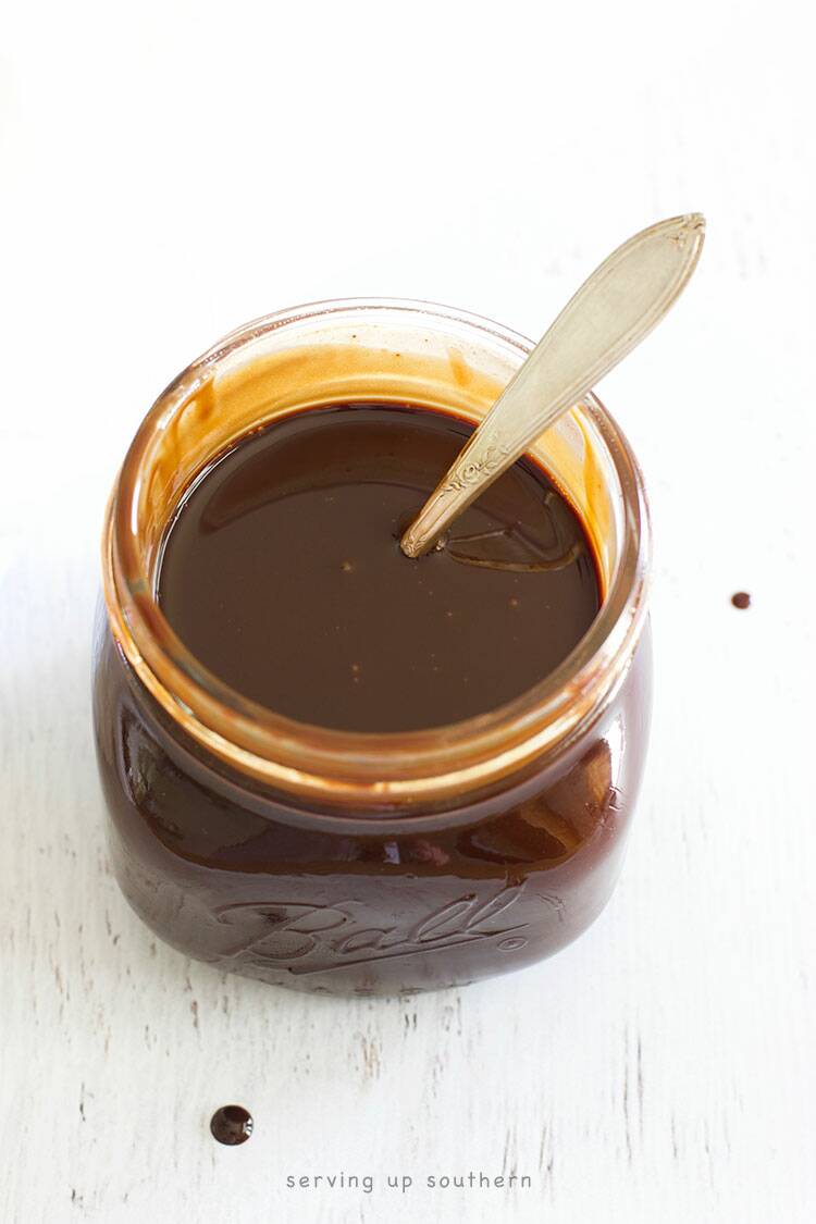 A half-pint mason jar filled to the brim with homemade chocolate syrup sitting on a white wood board.