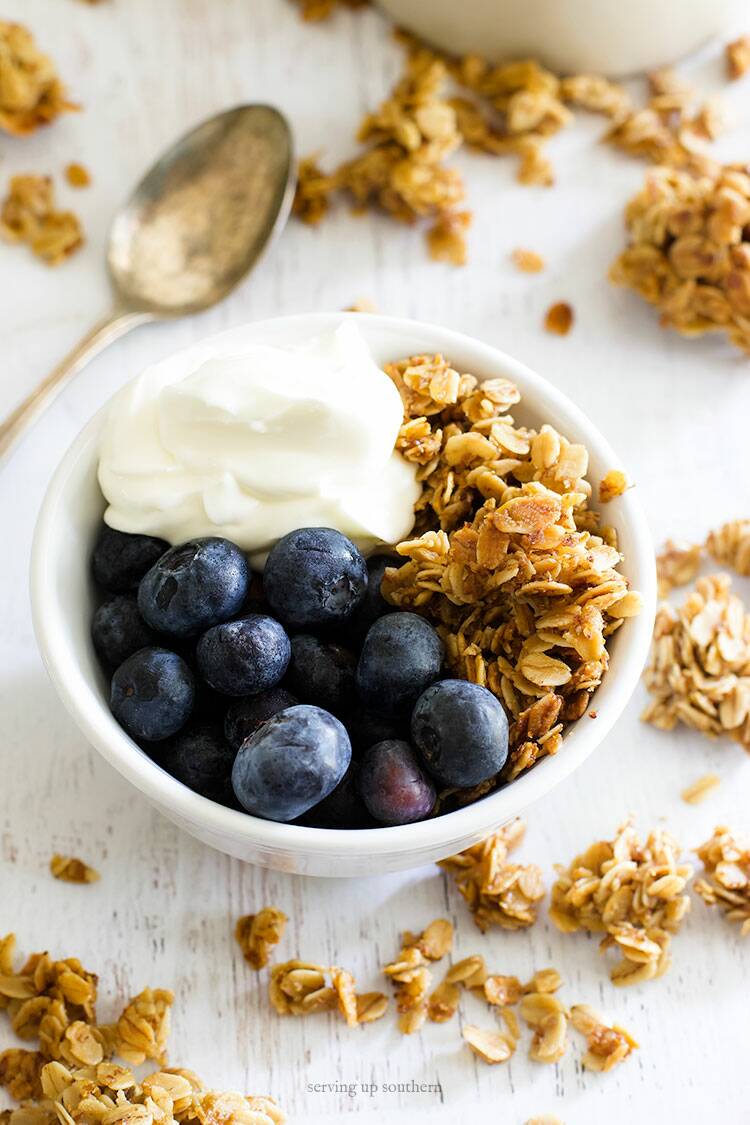 Picture of homemade granola, greek yogurt, and blueberries in a white bowl with a vintage silver spoon.