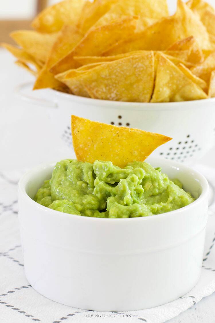 A white bowl of guacamole with one chip stuck in the center.