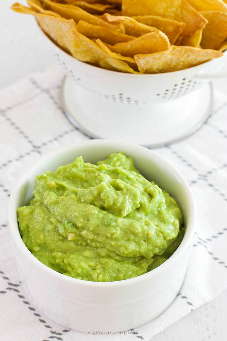 A white dish filled with guacamole with a side of chips.