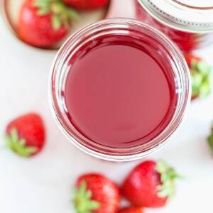 Jelly jar filled with homemade strawberry simple syrup with fresh strawberries scattered about.