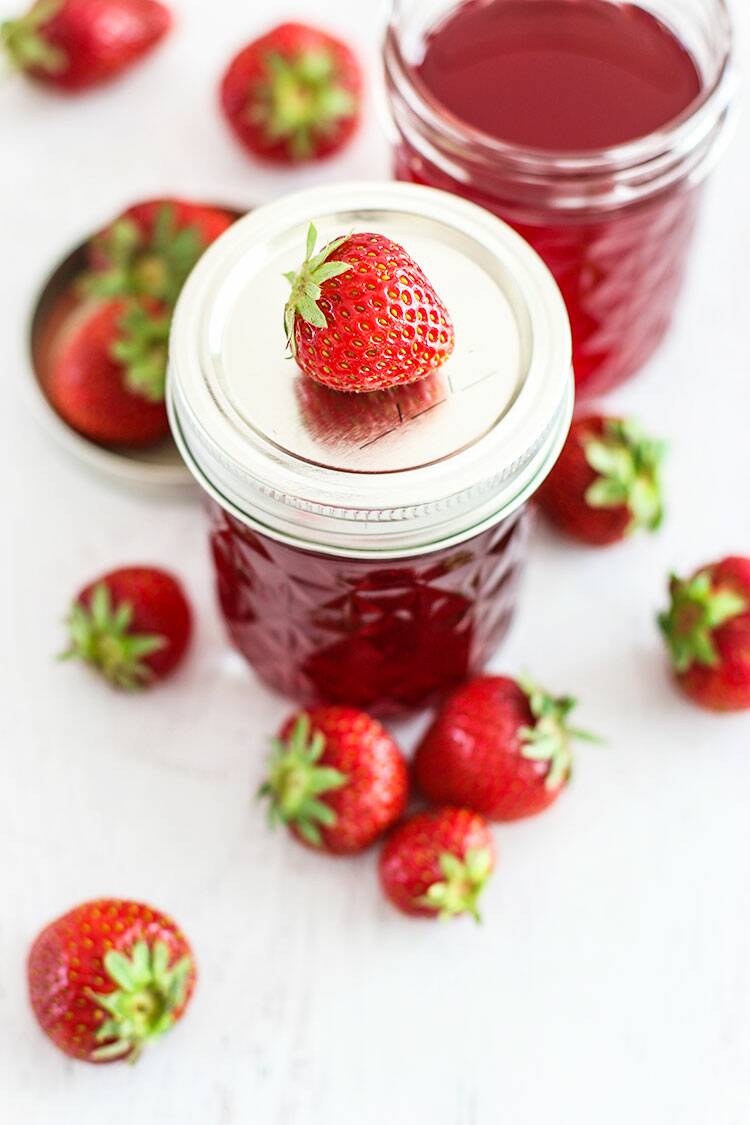 Simple syrup in a jelly jar with the lid on and a fresh strawberry on top.