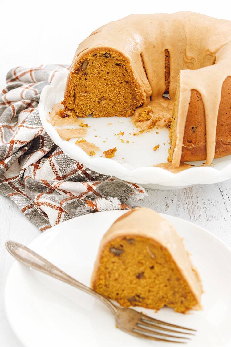 A slice of Pumpkin Bundt Cake on a white plate and silver fork on a white wood background.