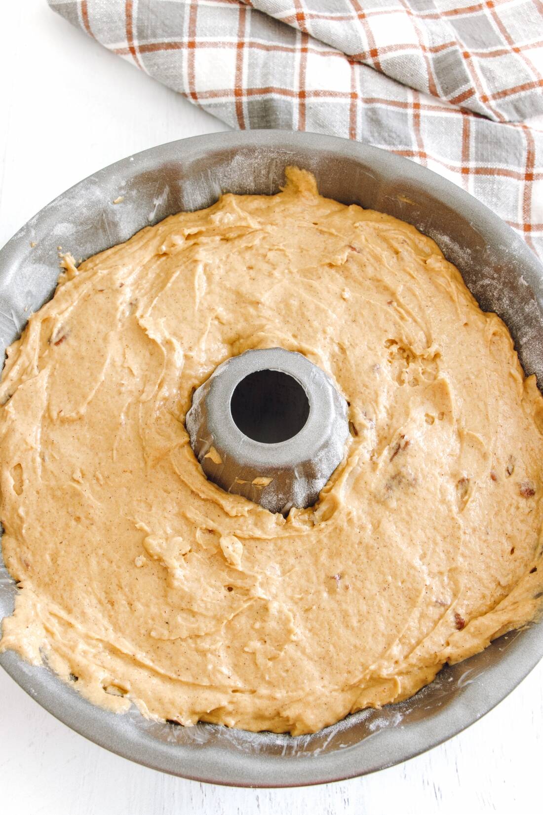 Pumpkin Bundt Cake - Bundt pan filled with cake batter sitting on white wooden board.