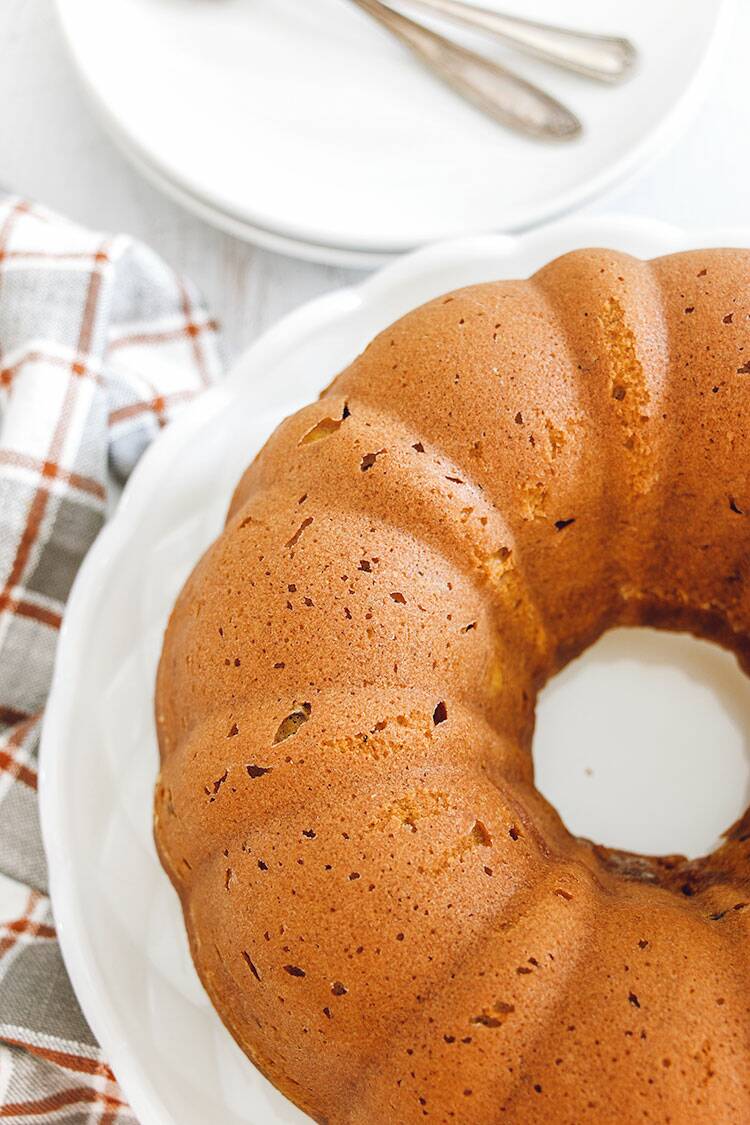 Pumpkin Bundt Cake on a white cake stands sitting on white wooden board with a dish towel.