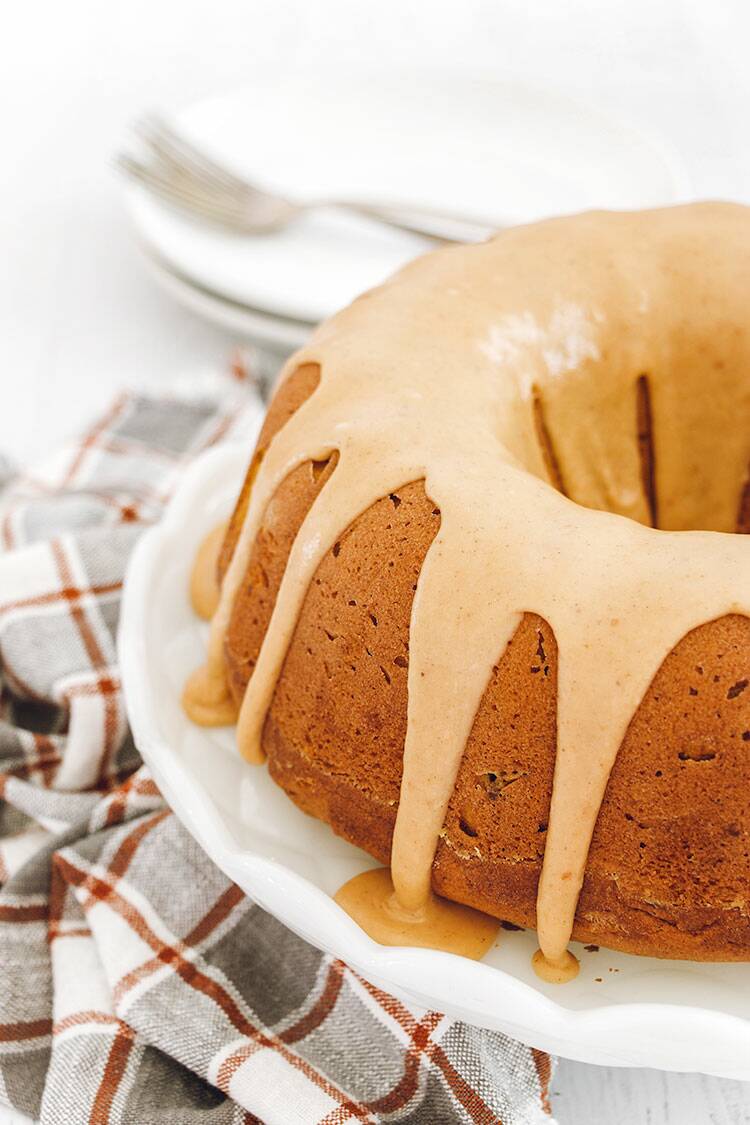 Pumpkin Bundt Cake drizzled with pumpkin spice glaze on a white cake plate.