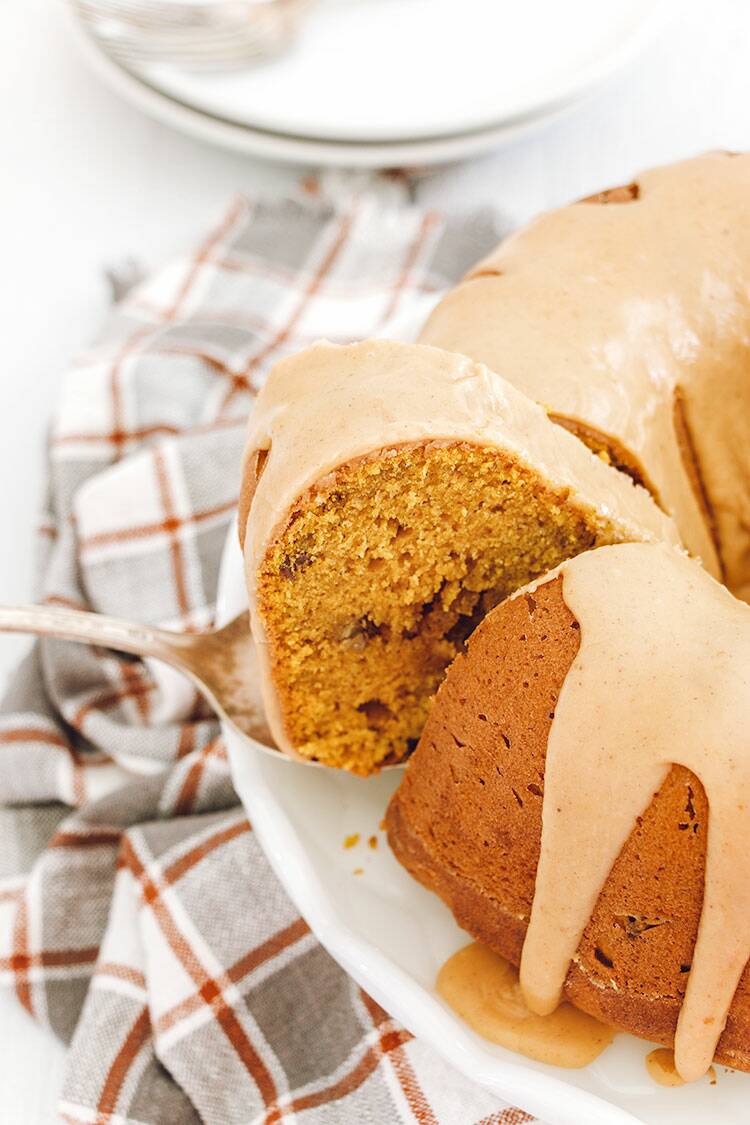 Pumpkin Bundt Cake slice being lifted from cake after being cut with a plaid dish towel in the background.