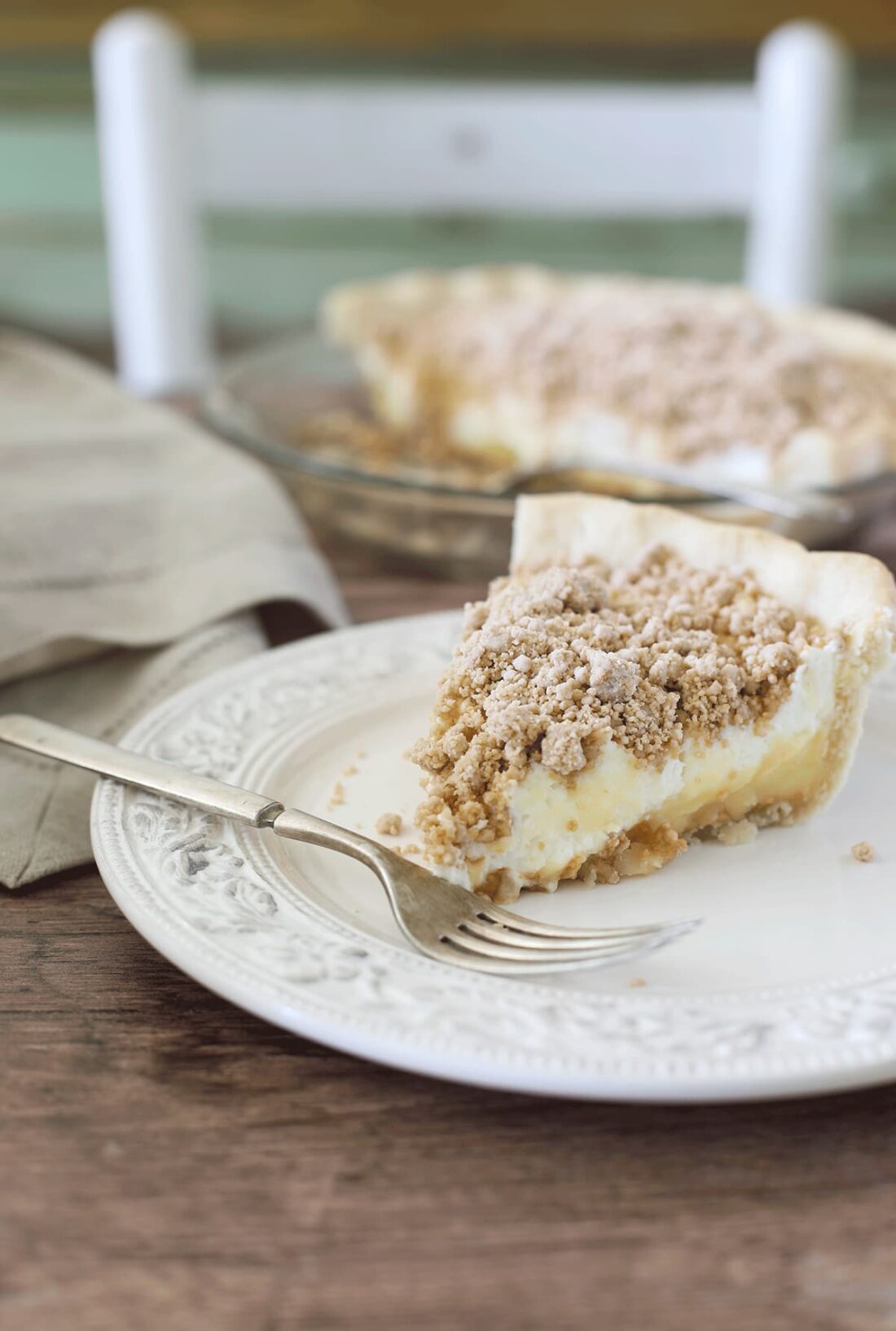 Slice of old fashioned peanut butter pie on a white dessert plate with a fork and napkin set on a rustic wooden surface.