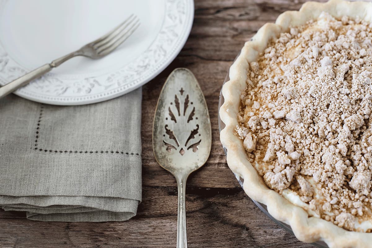 Old Fashioned Peanut Butter Pie on a rustic wooden board with a white plate, pie server, fork, and napkin.