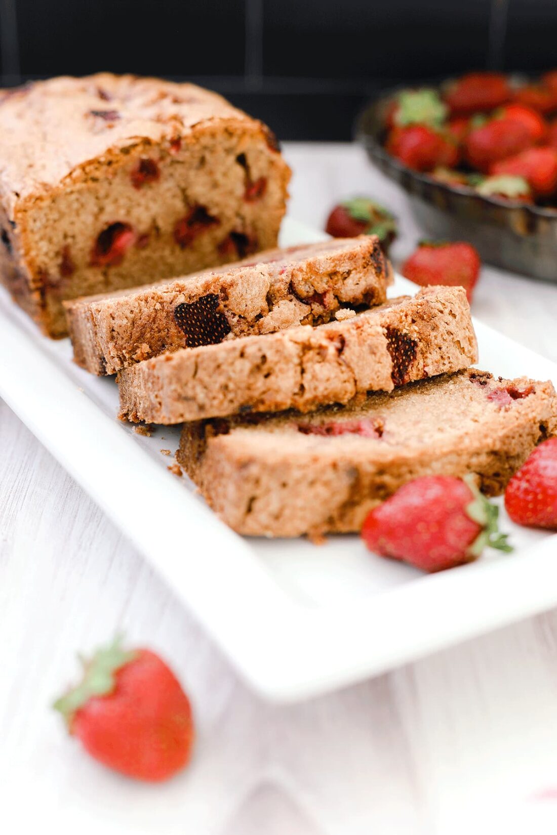 Strawberry bread on a while plate sitting on a wooden board with strawberries in the background.