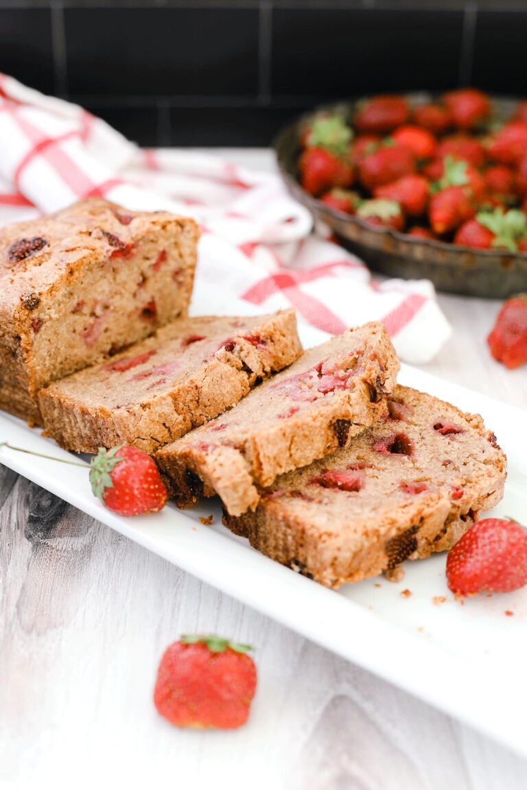 Strawberry bread on a while plate sitting on a wooden board with strawberries in the background.