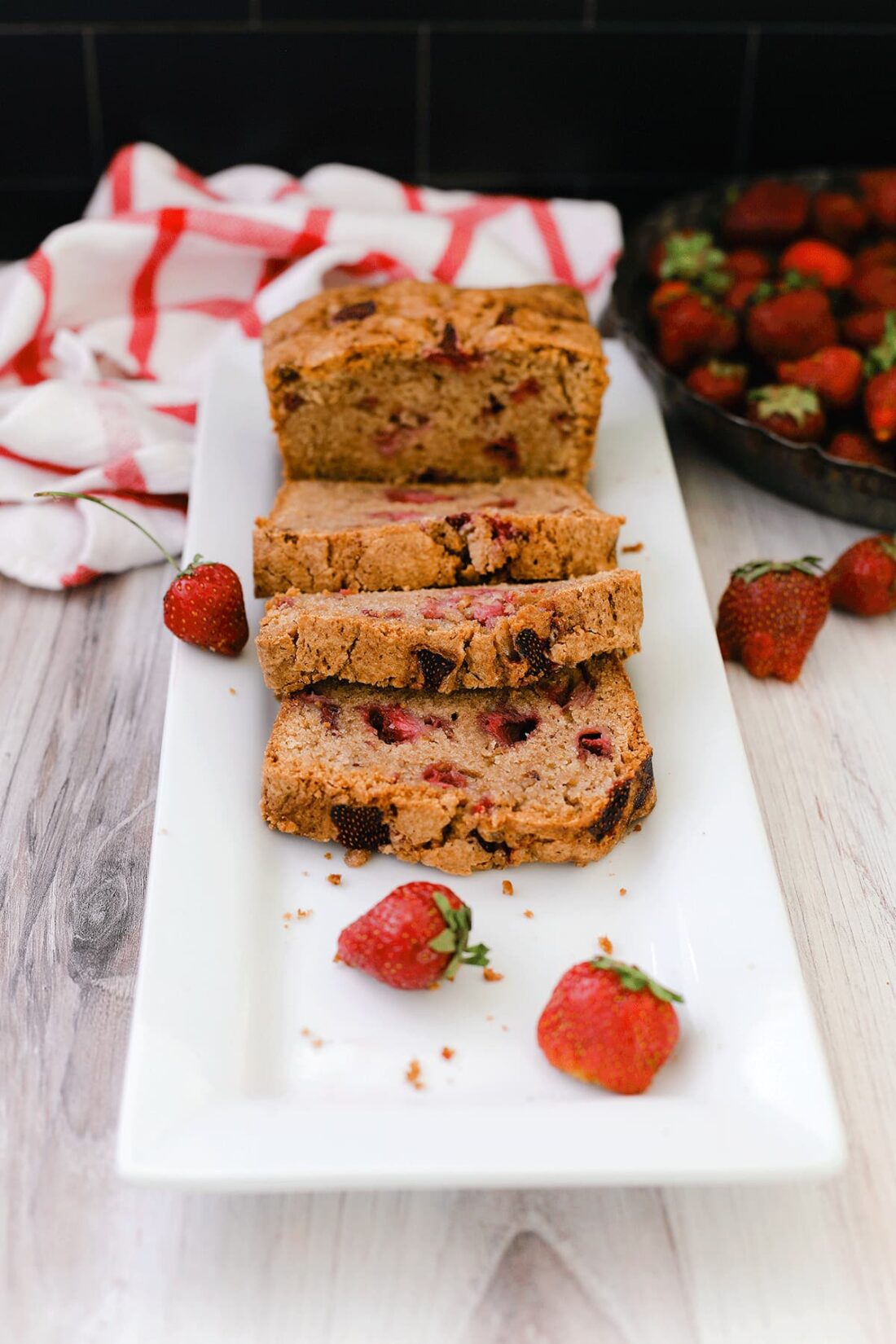 Strawberry bread on a while plate sitting on a wooden board with strawberries in the background.