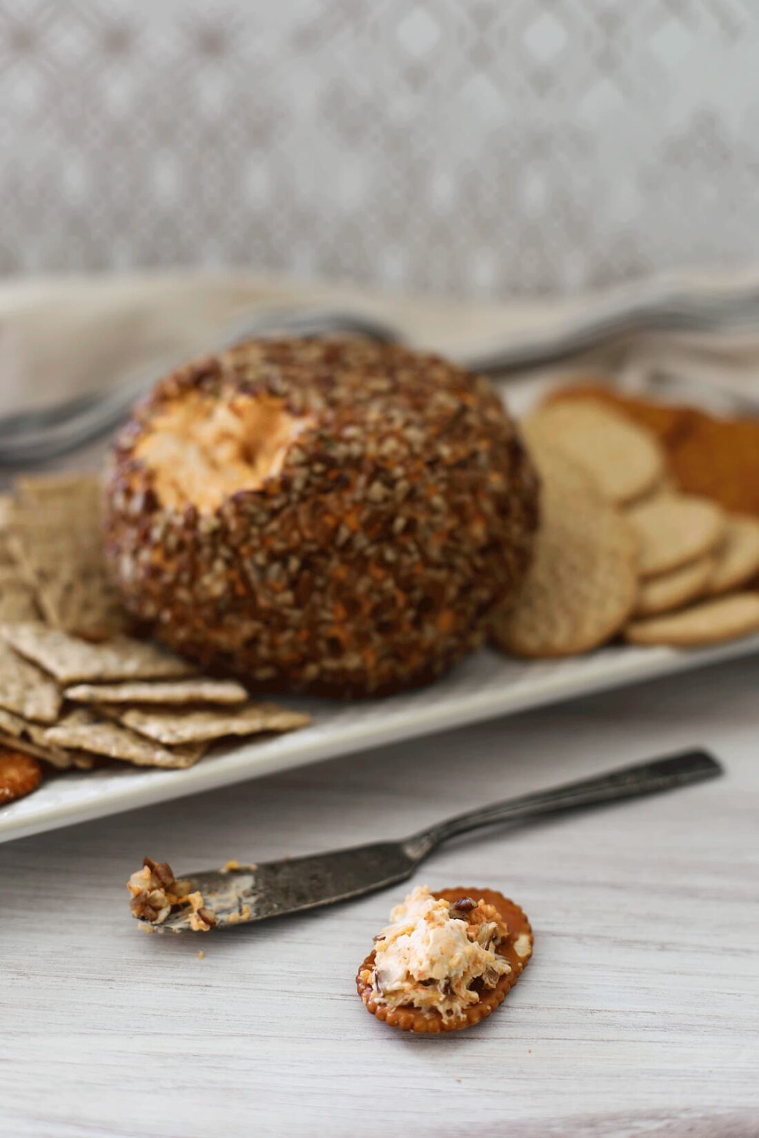 Cheese ball on a white plate with crackers on a white board.