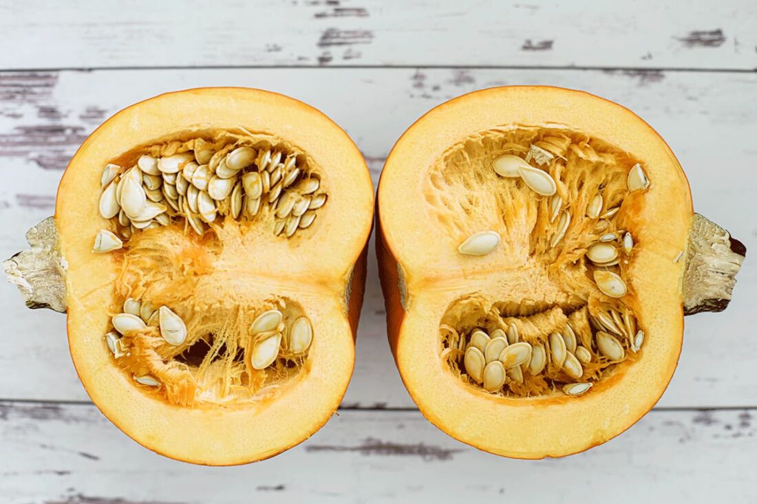 Sugar pumpkin cut in half exposing the seeds inside on a white wooden board.