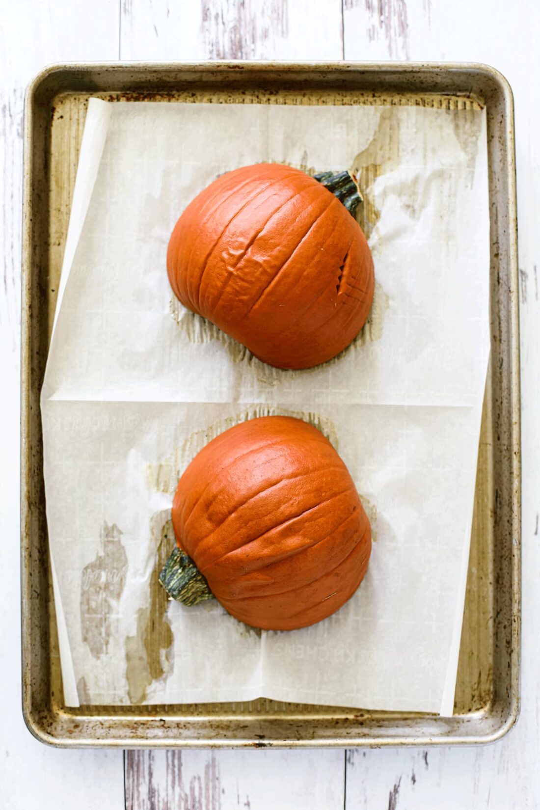 Baked sugar pumpkin halves on a parchment paper-lined sheet pan.