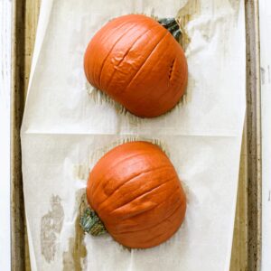 Cooked sugar pumpkin halves on a parchment paper-lined sheet pan.