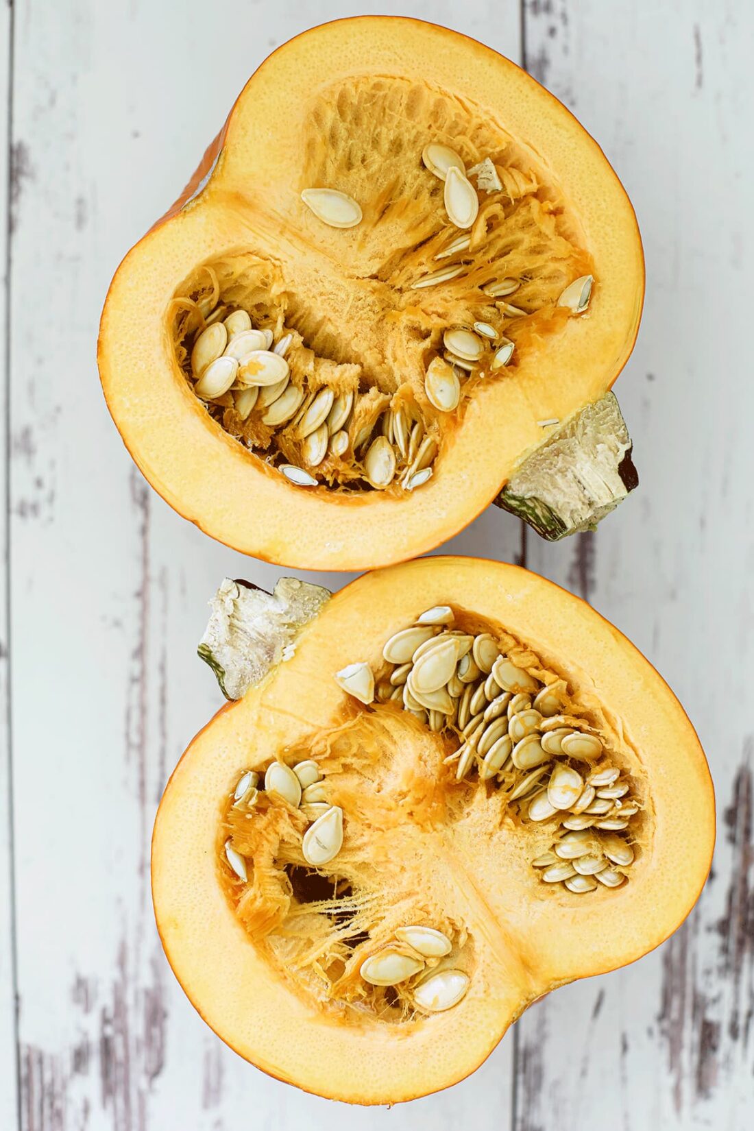 Sugar pumpkin cut in half exposing the seeds inside on a white wooden board.