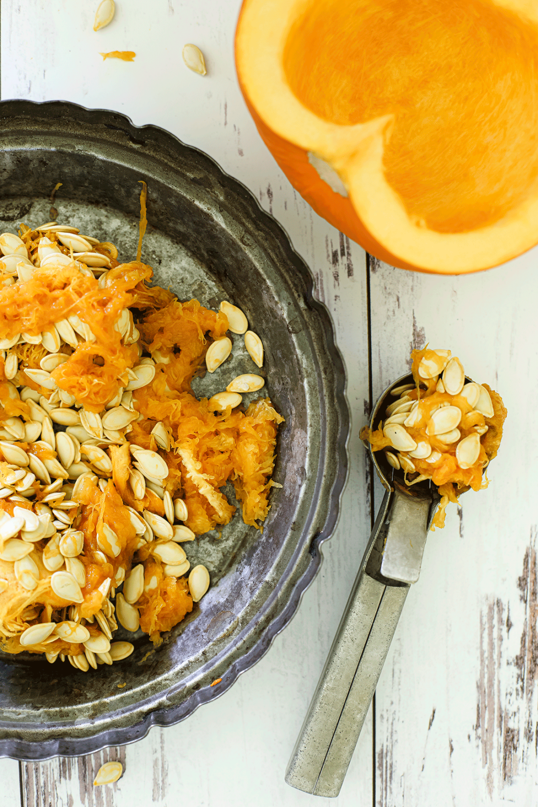 One half of a pumpkin being scooped out with an ice cream scoop.