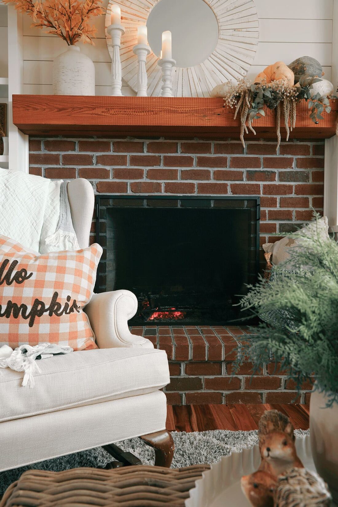 Picture of fireplace decorated with pumpkins and candles. And a cozy chair pulled up by the fire.